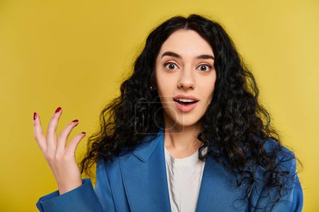 A young brunette woman with curly hair exhibits a surprised expression, showcasing her emotions in a studio with a vibrant yellow backdrop.