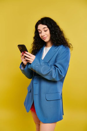 Téléchargez les photos : Une jeune femme dans un blazer bleu captivé par son téléphone portable, intensément concentré sur l'écran. - en image libre de droit