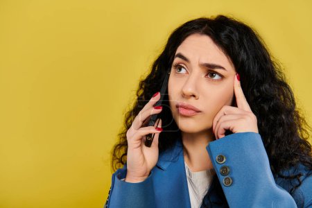 Photo for A brunette woman with curly hair in stylish attire holds a cell phone to her ear, showing various emotions against a yellow background. - Royalty Free Image
