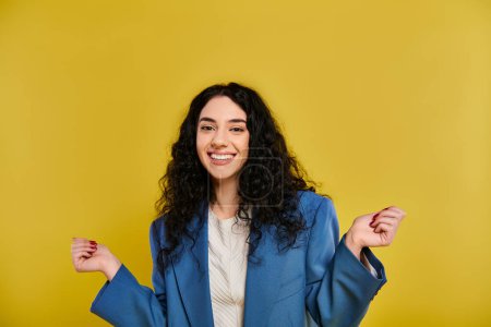 Foto de Una joven con el pelo rizado posa elegantemente en una chaqueta azul y una camisa blanca, mostrando sus emociones contra un fondo de estudio amarillo. - Imagen libre de derechos