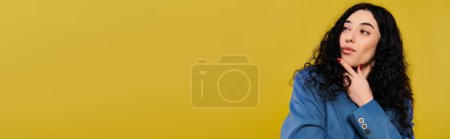 Foto de Joven morena de pelo rizado posa con confianza en una camisa azul en un estudio con un fondo amarillo vibrante. - Imagen libre de derechos