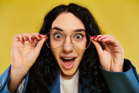 Photo for A young, stylish woman with curly hair wearing glasses is expressing surprise against a vibrant yellow backdrop. - Royalty Free Image