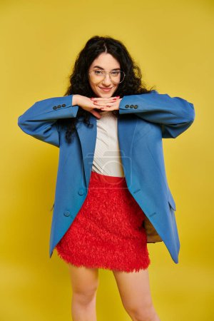 A young brunette woman with curly hair poses in a stylish blue jacket and red skirt, showcasing a range of emotions in a studio setting with a yellow background.