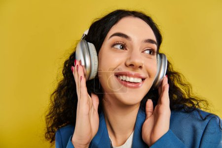 A young brunette woman with curly hair listens to music through headphones, lost in the rhythm against a vibrant yellow backdrop.
