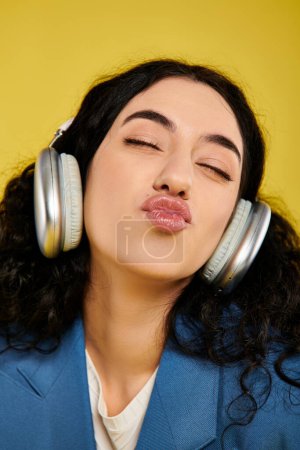 Eine junge Frau mit lockigem Haar schließt die Augen, während sie in einem Studio mit gelbem Hintergrund Kopfhörer trägt.
