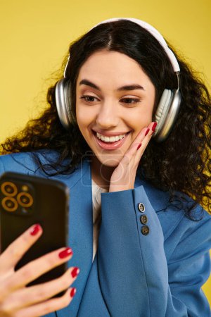 Una mujer joven con el pelo rizado, con auriculares y mirando un teléfono celular, inmersa en el mundo de la música y la comunicación.