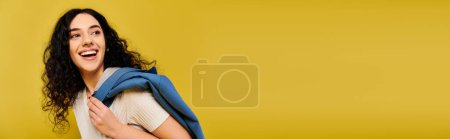 Foto de A stylish young woman with curly hair captured against a bright yellow background. - Imagen libre de derechos
