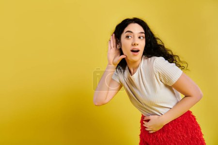 Eine brünette Frau mit lockigem Haar sieht überrascht aus, in stilvoller Kleidung, in einem Studio mit gelbem Hintergrund.