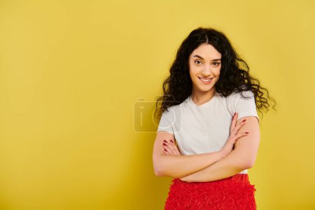 Téléchargez les photos : Une jeune femme brune aux cheveux bouclés se tient avec confiance les bras croisés sur un fond jaune vif. - en image libre de droit