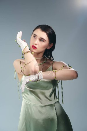 A young beautiful woman with red lips poses in a green dress, white gloves in a studio setting on a grey background.