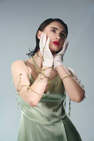 A young woman with red lips strikes a pose in a green dress and white gloves in a studio setting, exuding an enchanting presence.
