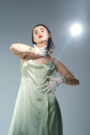 Photo for A beautiful young woman with red lips poses in a green dress and white gloves in a studio setting against a grey backdrop. - Royalty Free Image