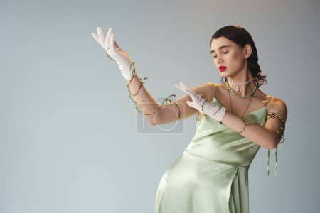 Téléchargez les photos : Une jeune et belle femme aux lèvres rouges pose dans une superbe robe vert émeraude et gants blancs dans un décor studio. - en image libre de droit