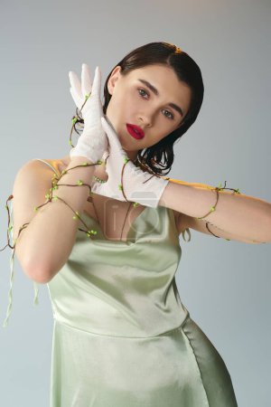 Photo for A young, beautiful woman with red lips strikes a pose in a green dress and white gloves in a studio setting on a grey backdrop. - Royalty Free Image