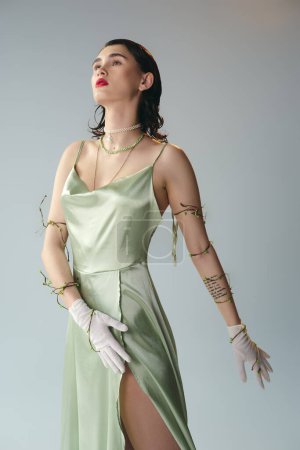 A young, beautiful woman with red lips is posing in a luxurious green dress and elegant white gloves in a studio setting on grey.