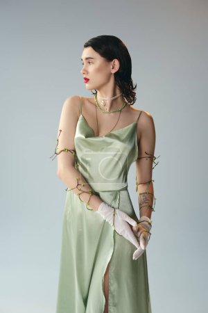 A young, beautiful woman with red lips poses in a vibrant green dress and gloves in a studio setting against a grey backdrop.