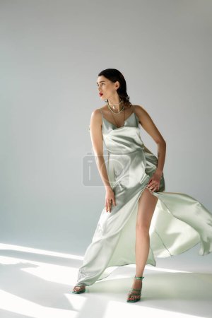 Photo for A young woman with red lips strikes a pose in a flowing dress and gloves, set against a grey studio backdrop. - Royalty Free Image