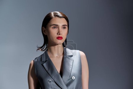 A stylish young woman with red lipstick stands confidently in front of a gray background, exuding elegance and charm.