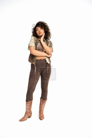 Téléchargez les photos : Femme afro-américaine sophistiquée en tenue avec impression animalière sur fond blanc regardant loin - en image libre de droit