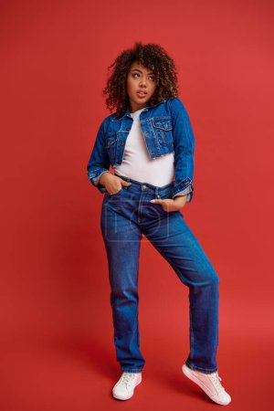 Photo for Well dressed young african american woman in stylish denim outfit looking away on red backdrop - Royalty Free Image