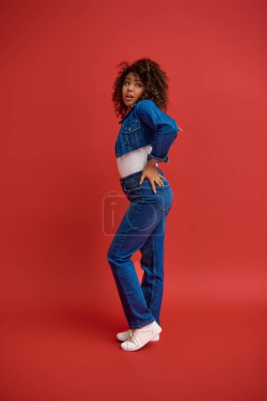 Photo for Graceful young african american woman in stylish denim outfit looking away on red backdrop - Royalty Free Image