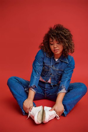 Photo for Good looking young african american woman in stylish denim outfit looking away on red backdrop - Royalty Free Image