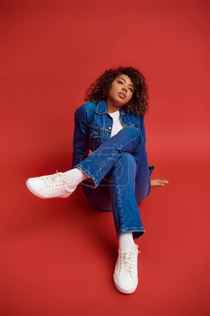 Photo for Alluring young african american woman in stylish denim outfit looking away on red backdrop - Royalty Free Image