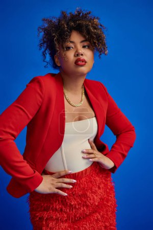 Photo for Graceful african american woman in red skirt and blazer on blue backdrop and looking at camera - Royalty Free Image