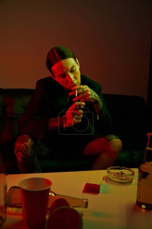 Téléchargez les photos : Un homme assis sur un canapé fumant une cigarette - en image libre de droit