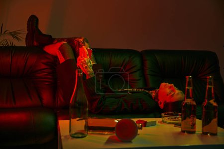 Photo for Man reclining on a couch next to a table in a room - Royalty Free Image