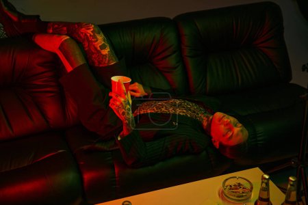 A person laying comfortably on a couch, holding a drink in their hand