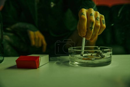 Individual sentado en la mesa con el cigarrillo descansando en un vaso