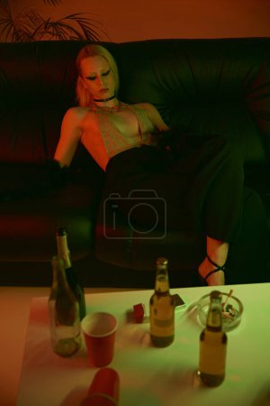Téléchargez les photos : Une femme est assise sur un canapé à côté de diverses bouteilles d'alcool - en image libre de droit