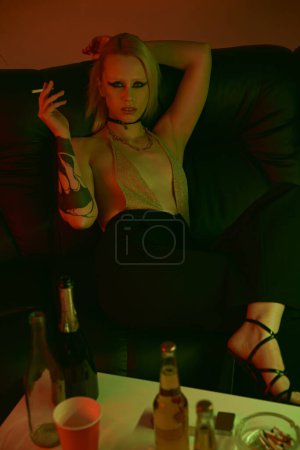 Téléchargez les photos : Une femme assise sur un canapé, fumant une cigarette - en image libre de droit
