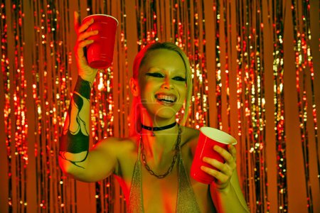 Eine geschminkte Frau hält bei einer Rave-Party zwei Tassen hoch