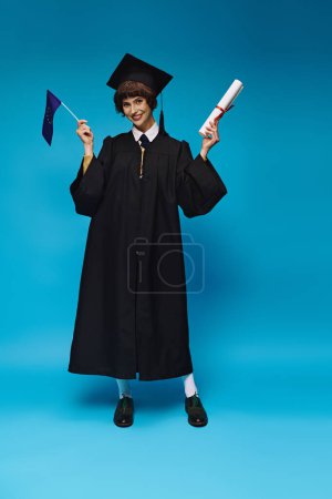alegre graduado chica universitaria en vestido y gorra académica con diploma y bandera de la UE sobre fondo azul