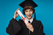 cheerful college girl in gown and academic cap holding her diploma with pride on blue, graduation Longsleeve T-shirt #712417778