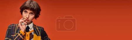 student with short hair posing in stylish checkered blazer on orange background, college girl banner