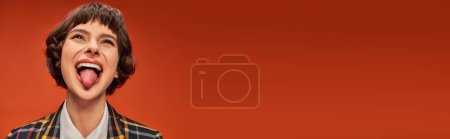 Photo for Playful female student in college uniform sticking out tongue, lively on orange background, banner - Royalty Free Image