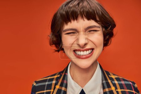 Fröhliches College-Mädchen mit strahlendem Lächeln, das ihre weißen Zähne vor leuchtend orangefarbenem Hintergrund zeigt