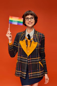 joyful young college girl in uniform and glasses holding lgbt flag and standing on orange background puzzle #712419052
