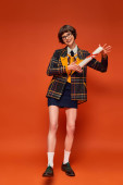 excited graduate college girl in uniform and glasses holding her diploma on vibrant orange backdrop Tank Top #712419560