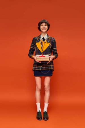 full length of positive student in college uniform standing with books on orange background mug #712420016