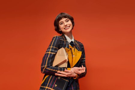 portrait of happy student in college uniform standing with books on orange background, knowledge
