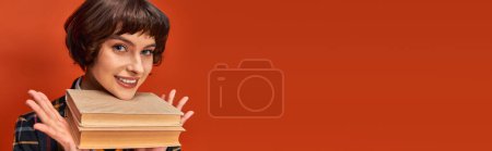 banner of smiling college girl in uniform holding books near chin on orange background, knowledge mug #712420112