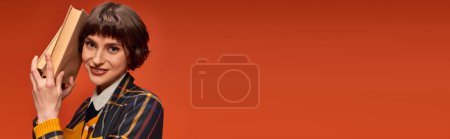banner of cheerful college girl in uniform holding books near face on orange background, knowledge tote bag #712420180