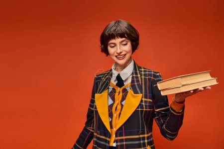 happy college girl in uniform holding stack of books in hand on orange background, knowledge magic mug #712420268