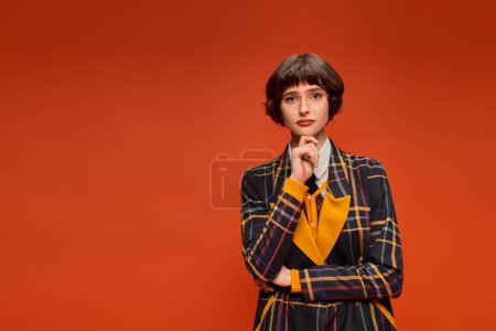 Photo for Thoughtful college girl with short hair posing in checkered uniform on orange background, decision - Royalty Free Image