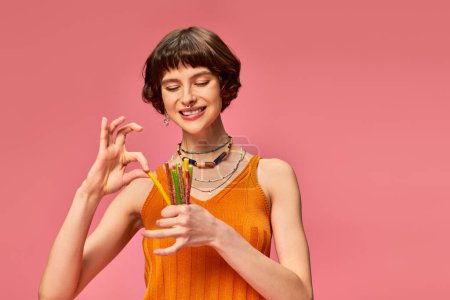 Téléchargez les photos : Heureux percé femme dans son 20s sourire et tenant tas de bonbons aigre-doux dans les mains sur rose - en image libre de droit