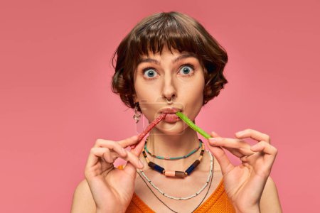 Foto de Divertido perforado chica en su 20s comer dos sabores diferentes de dulces y amargos caramelos en rosa - Imagen libre de derechos